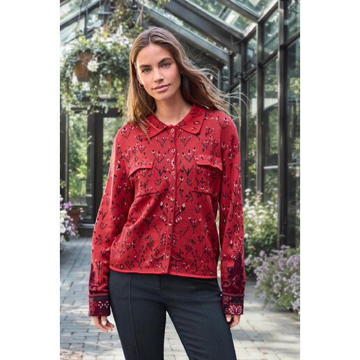 Frau in roter Jacquard-Strickbluse mit floralem Muster in einem Gewächshaus.