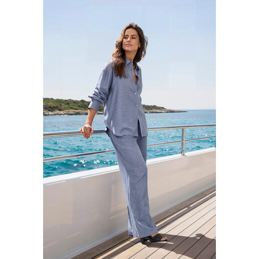 Frau in blauer Bluse und Hose steht auf einem Boot im Meer.