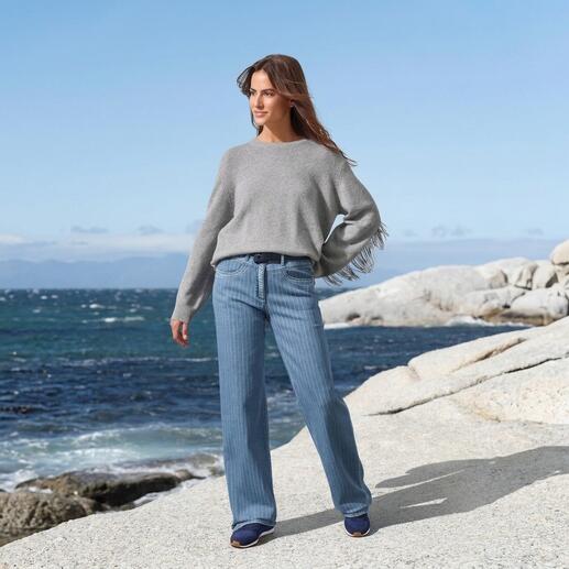 Grauer Pulli mit Fransen, lässig über Jeans getragen am Strand.