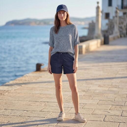 Frau steht am Meer in blauem Pulli und Shorts.
