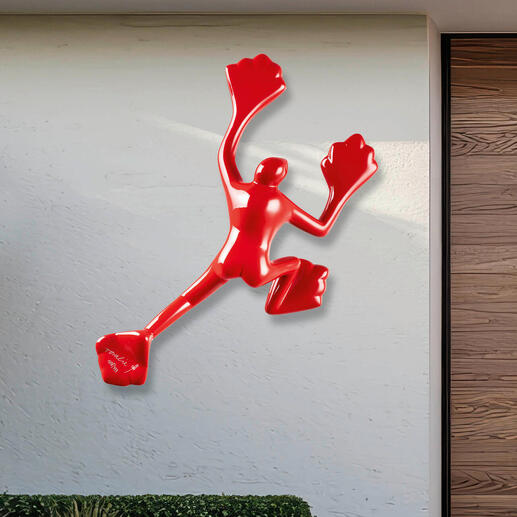 Rotere Skulptur an einer hellen Wand im Außenbereich.