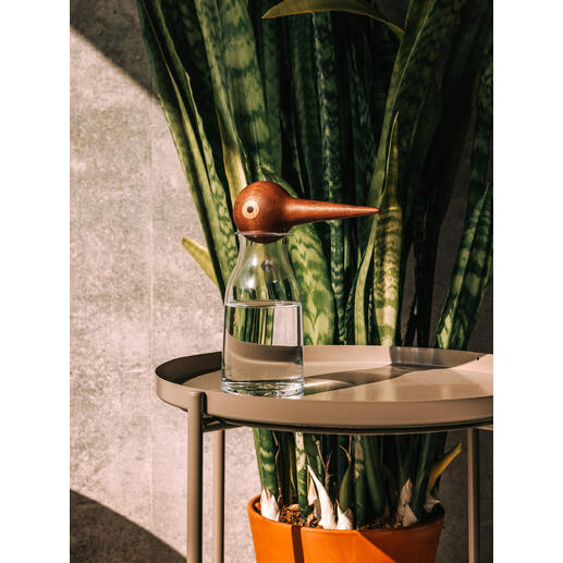 Glas wasser mit hölzernem Wasserspender in Form eines Vogels auf einem Tisch.