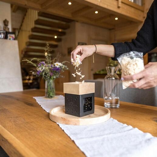 Person fügt Holzspäne in ein Zirbenholz-Kraftwerk auf einem Tisch ein.