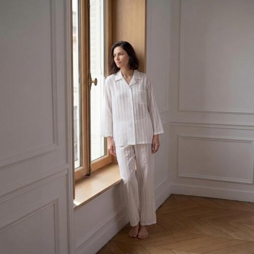Frau im Baumwoll-Seiden-Streifenpyjama steht am Fenster in einer eleganten Pose