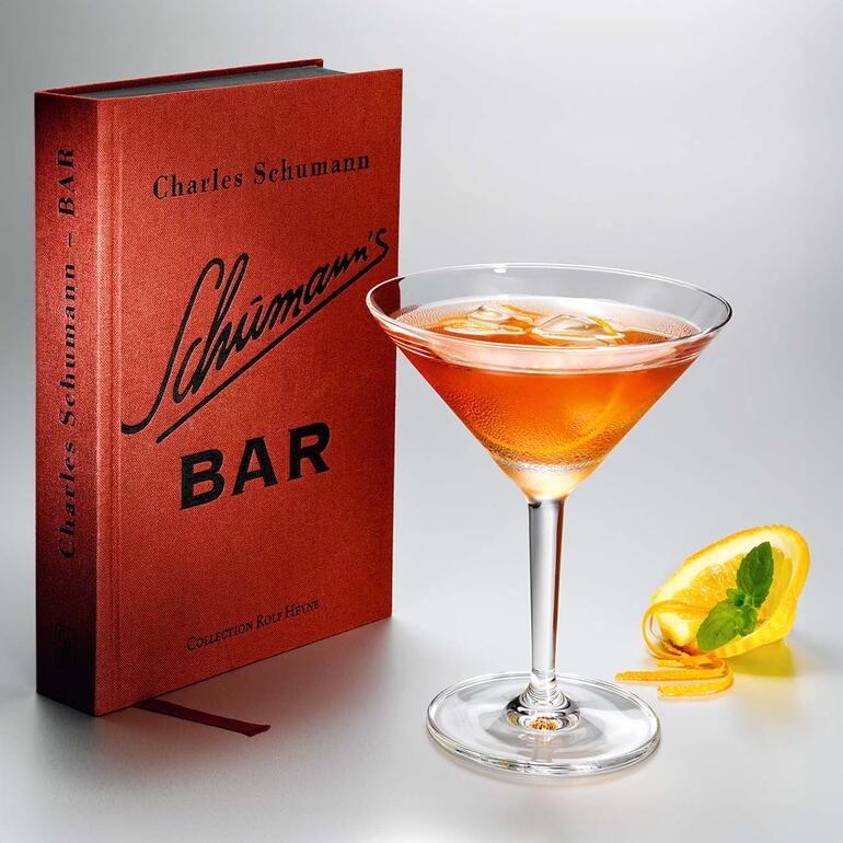 Martini-Glas mit Getränk vor einem Buch mit dem Titel 'Schumann's Bar'.