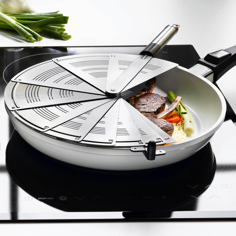 Spritzschutz-Fächer aus Edelstahl in einer Pfanne mit Fisch und Gemüse.