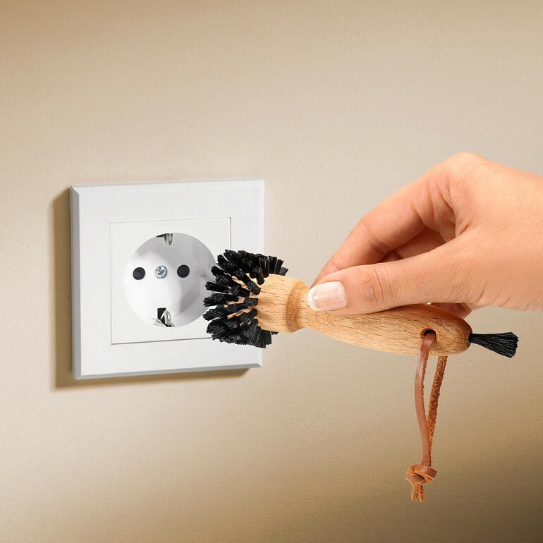 Hand benutzt eine Steckdosenbürste an einer Steckdose