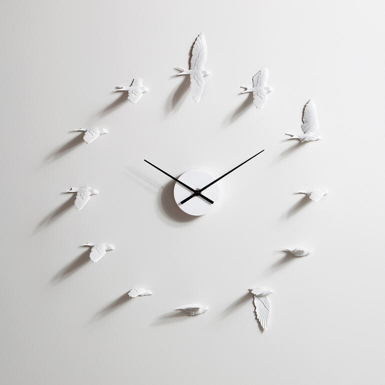 Moderne Wanduhr in Form von Schwalben, schwarze Zeiger auf hellem Hintergrund.