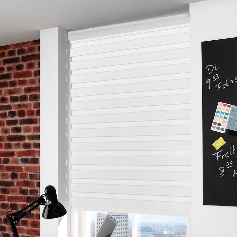 Weißes Rollo, das an einem modernen Fenster montiert ist, im Hintergrund sind Ziegelmauern sichtbar.