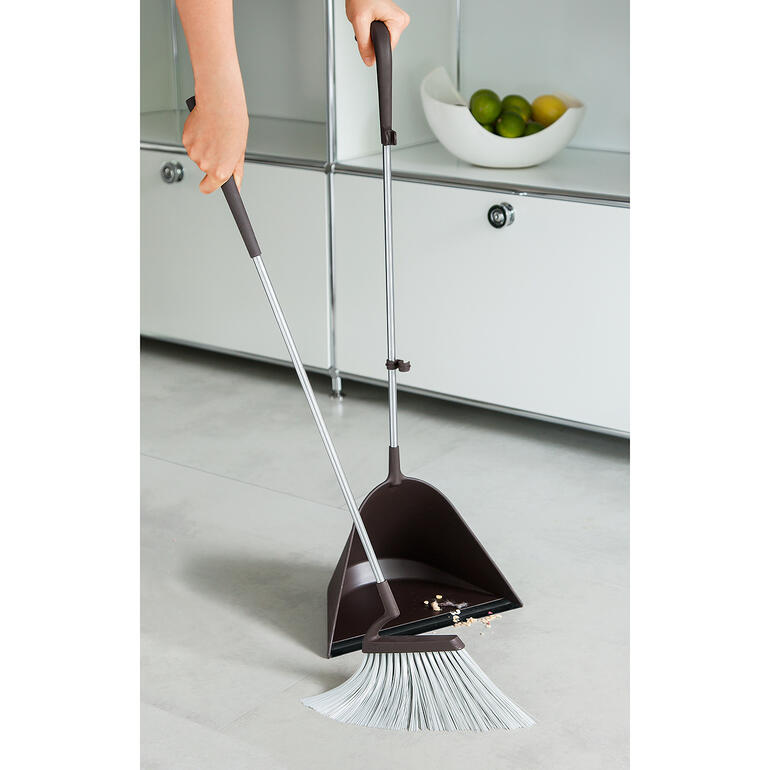Person mit TIDY Kehrset, fegt den Boden in einem modernen Raum.