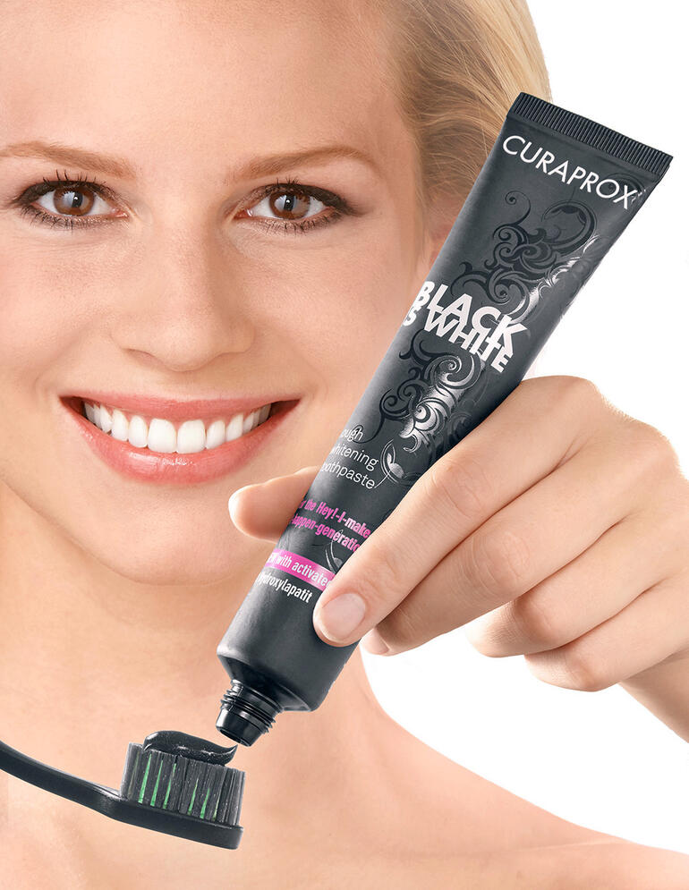 Frau hält eine Zahnbürste mit schwarzer Whitening-Zahncreme in der Hand, lächelt.