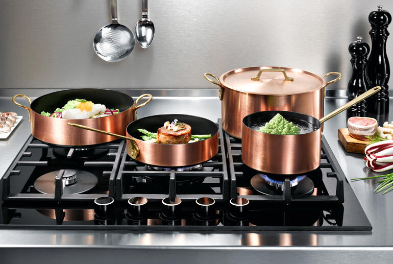 Induktions-Kupfer-Kochgeschirr auf einem Herd mit verschiedenen Töpfen und einer Pfanne.