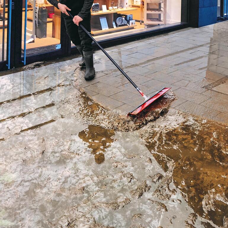 Mann mit Besen, der Wasser von einem Gehweg kehrt.