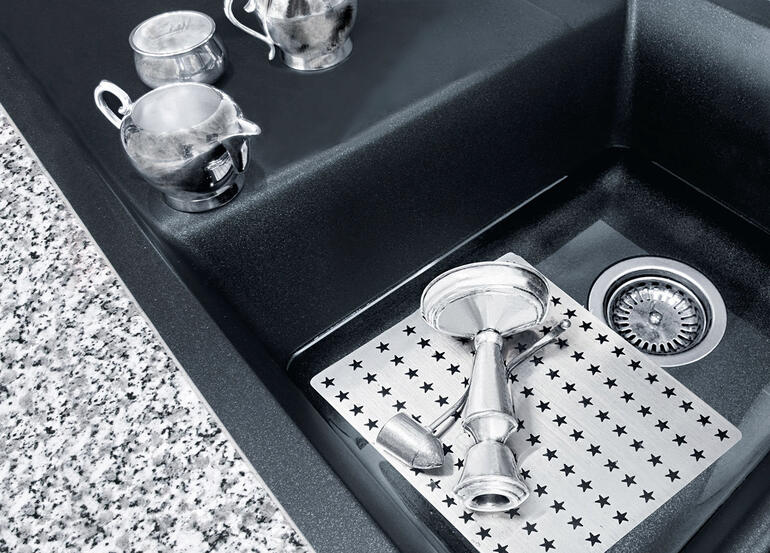 Reinigungsplatte auf einer Spüle mit Edelstahl-Töpfen.