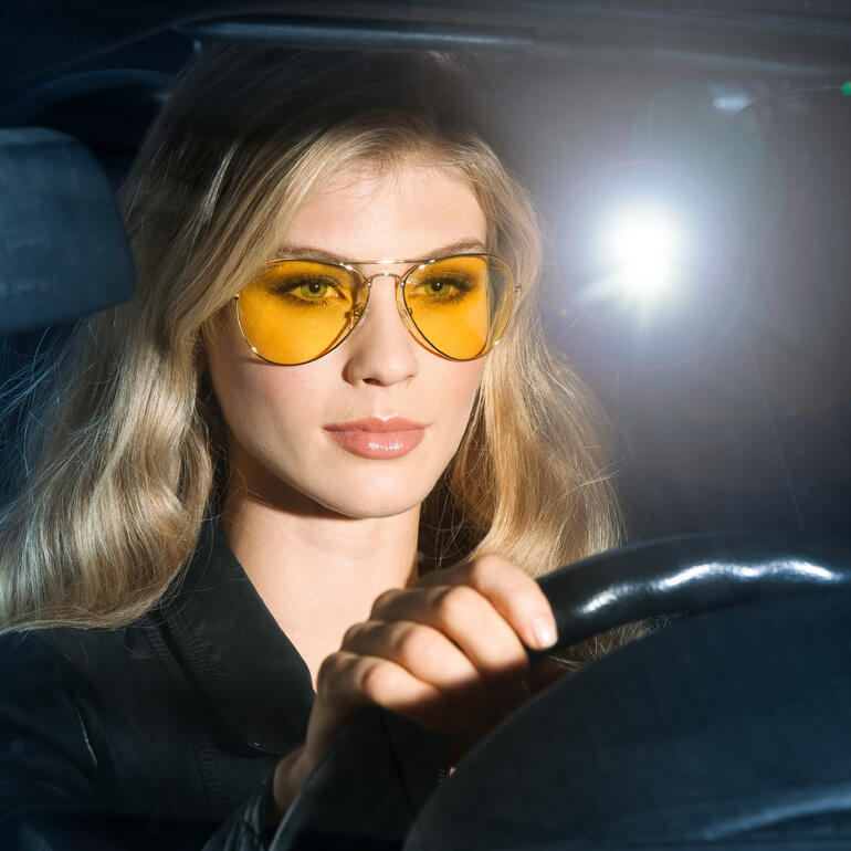 Eagle Eyes® Nacht-Brille oder Nacht-Brillenaufsatz Frau mit gelben Nacht-Brillenaufsatz am Steuer eines Autos.
