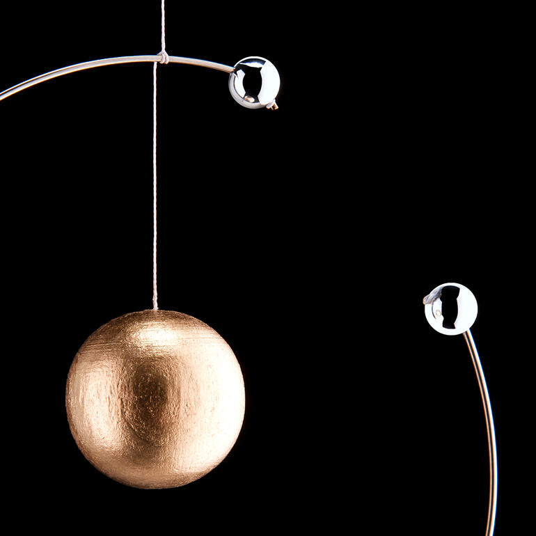 Mobile Niels Bohr Atommodell Nahaufnahme eines goldenen Balls im Atommodell, umgeben von silbernen Elektronen.