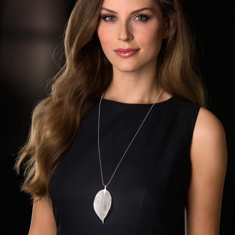 Frau trägt silberne Bodhi-Blatt-Kette auf schwarzem Hintergrund.