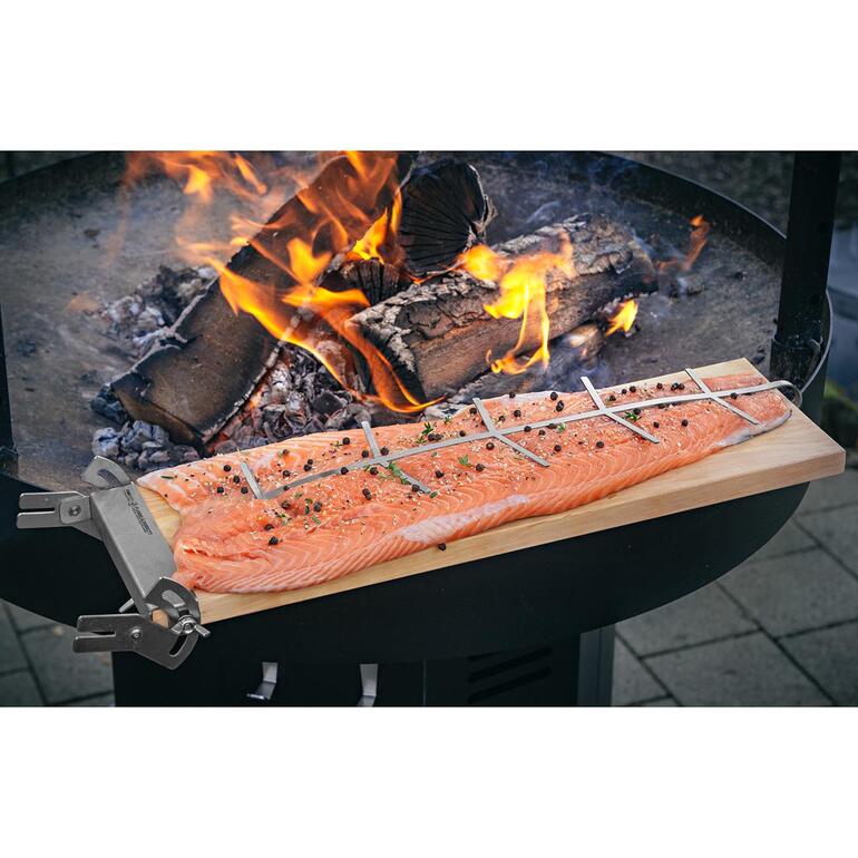 Lachsfilet auf einem Brett mit Kräutern über offenem Feuer gegrillt.