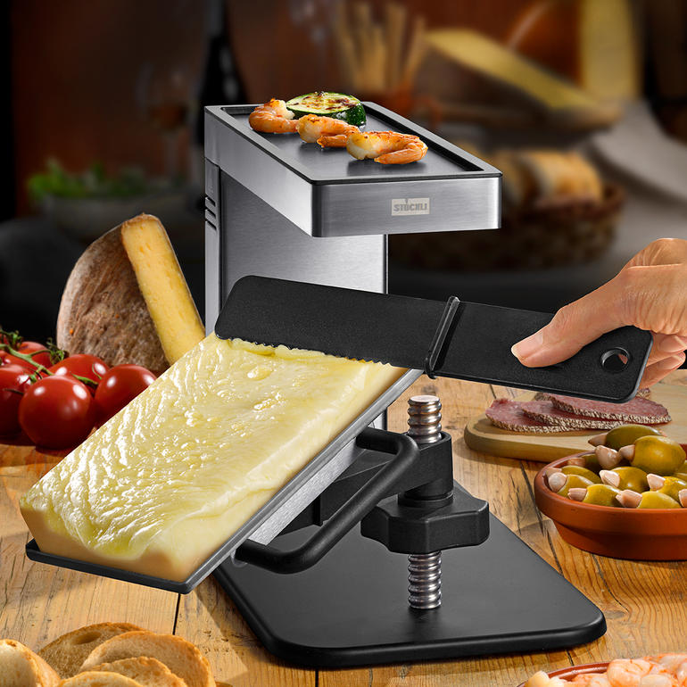 Raclette-Grill mit Stück Käse, Gemüse und Fisch auf der Grillplatte.