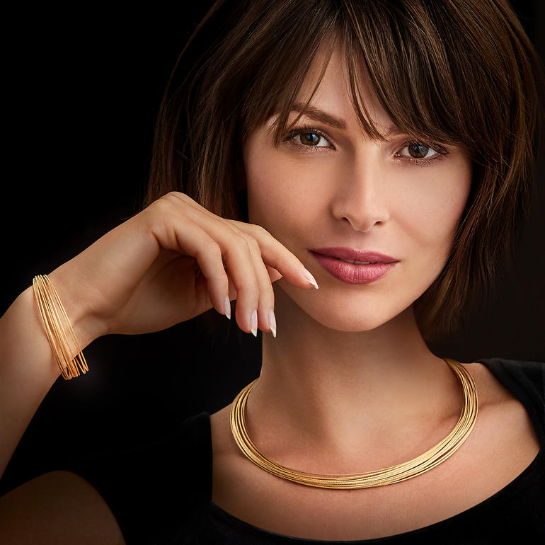 Frau mit Gold-Armband und Gold-Collier, lächelt in die Kamera