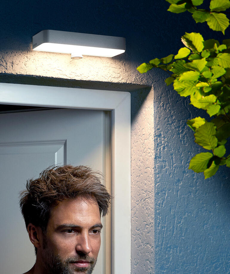 Mann steht unter einer Außen-Wandleuchte an der Tür.