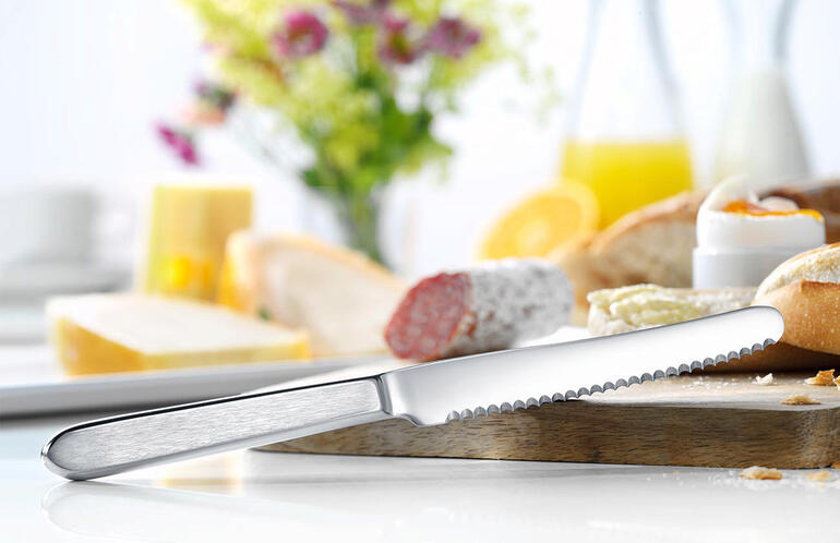 Brotzeitmesser aus Edelstahl auf einem Tisch mit Brot und Blumen.