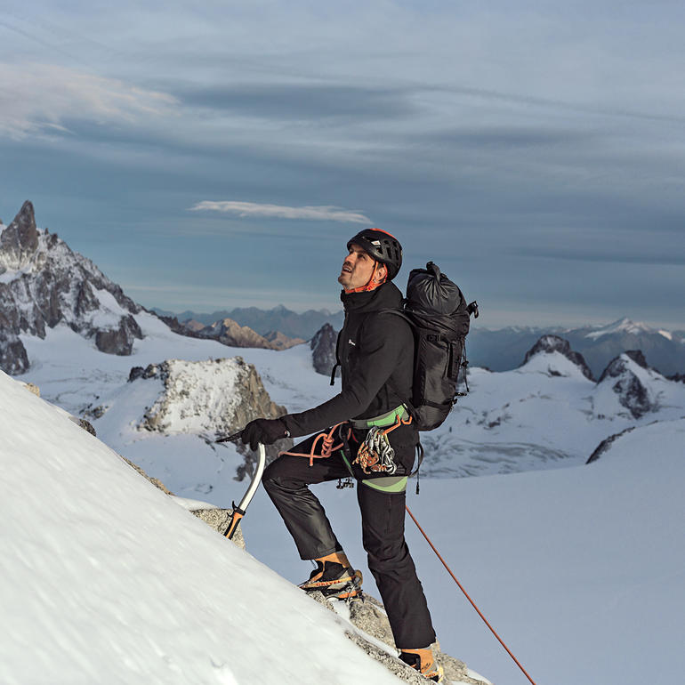 Mann in Berghaus ThinDown-Jacke beim Klettern auf einem Berg