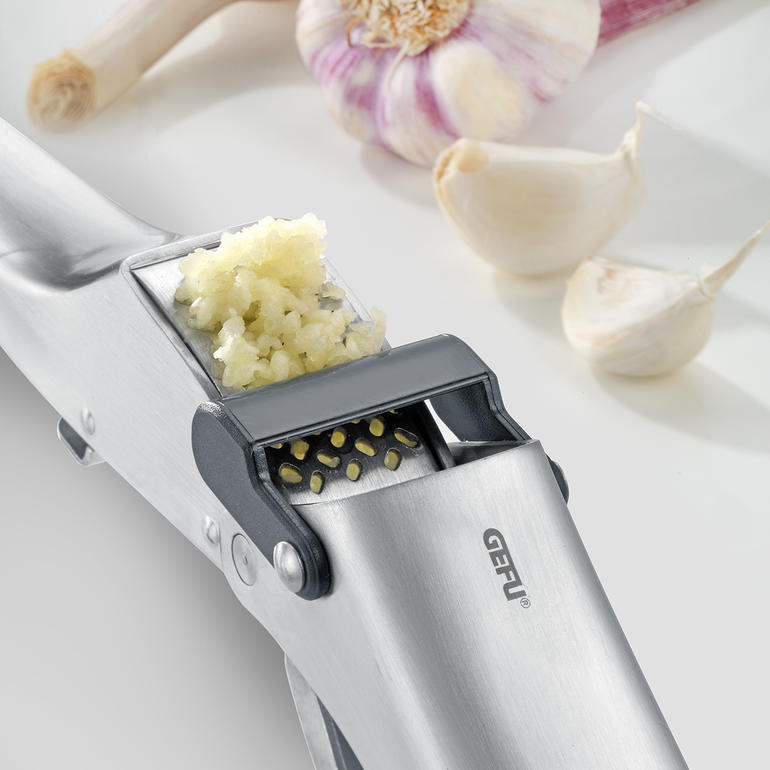 Knoblauchpresse mit zerdrücktem Knoblauch neben ganzen Zehen