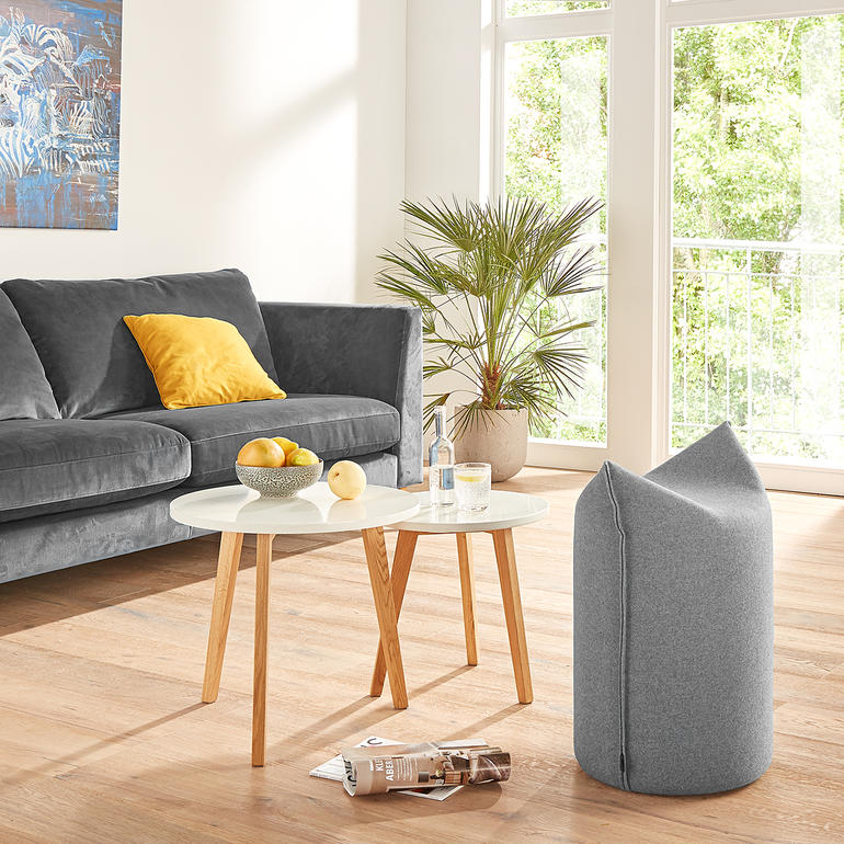 Zipfel-Hocker in grauem Stoff in Wohnzimmer mit Sofa und Tisch.