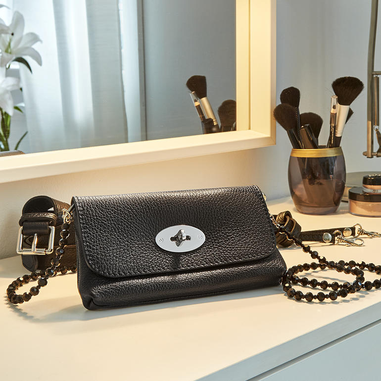 Schwarze Belt Bag aus Leder auf einem Schminktisch, mit Kosmetik.