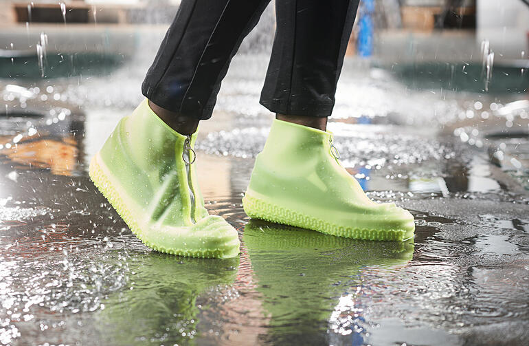 Person mit hellgrünen Regen-Überschuhen steht in einer Pfütze.