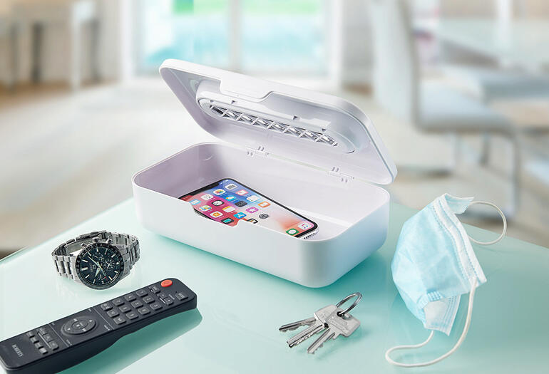 UV-C-Sterilisator 2-in-1 mit Smartphone und Alltagsgegenständen auf einem Tisch.