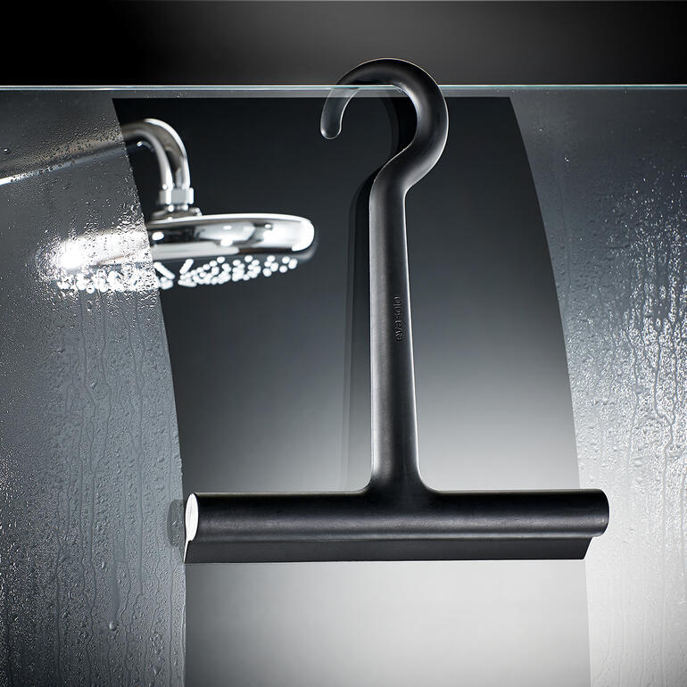 Design-Silikon-Duschabzieher hängt an einer Glasscheibe im Badezimmer.