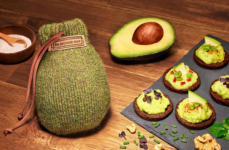 Avocado Sock® zusammen mit Avocado und Snacks auf einem Holztisch.