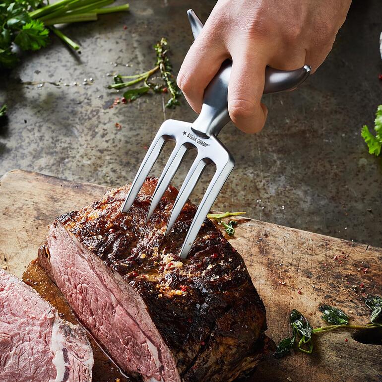 Hand hält Bull Fork, um ein Stück Fleisch zu schneiden.