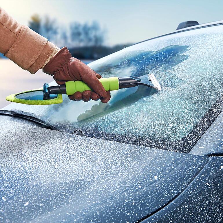 Hand mit Kombi-Scheibenreiniger beim Entfernen von Frost von der Autoscheibe