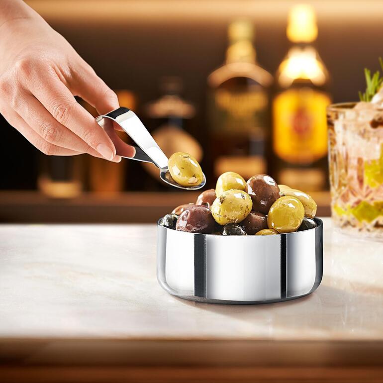 Design-Snackschale mit Löffel, gefüllt mit Oliven in einer Bar-Umgebung.