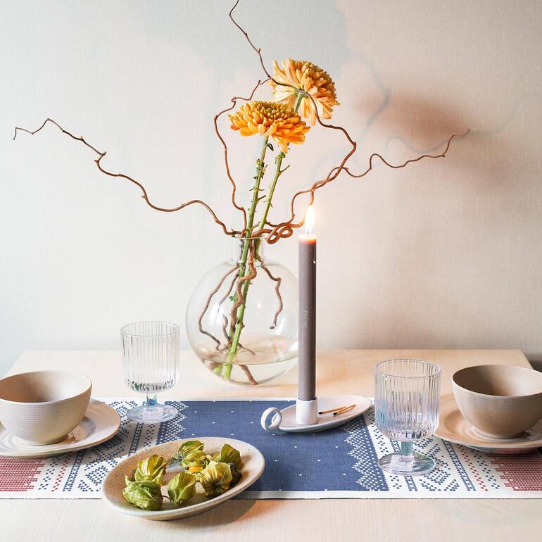 Tisch mit Tischläufer Norwegen, Kerze und Blumenarrangement.