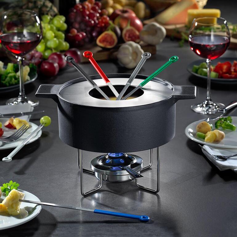 Mono Design-Fondue-Topf auf Tisch, umgeben von Zutaten und Wein.