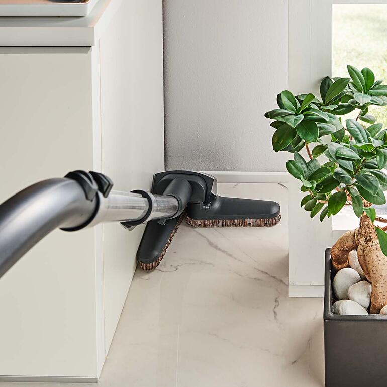 In Ecken und Nischen klappt die Flex-Düse sanft ein und wieder aus – lästiges Bücken und Möbelrücken wird überflüssig. Flexible Staubsaugerdüse, die in einer Ecke eines Raumes eingesetzt wird.