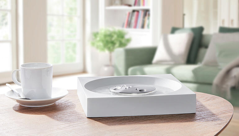 Geruchskiller XL auf einem Tisch mit Kaffee und einem Sofa im Hintergrund.