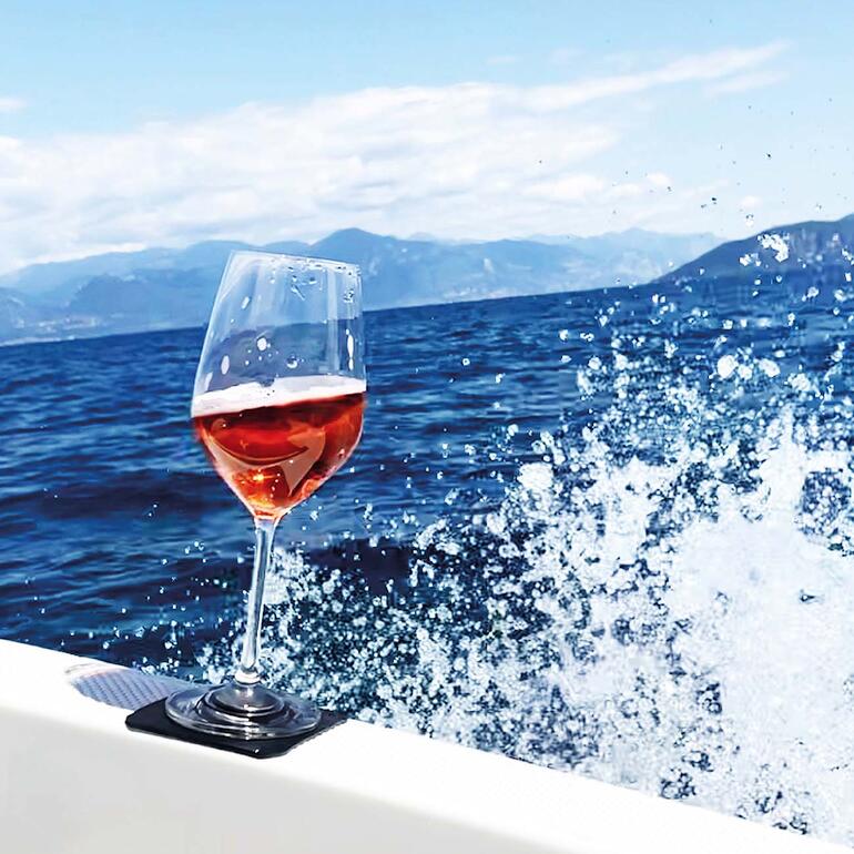 Weinglas mit Roséwein auf einem Boot vor einer malerischen Küstenlandschaft