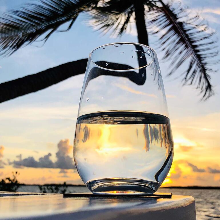 Glas mit klarem Wasser, Sonnenuntergang im Hintergrund