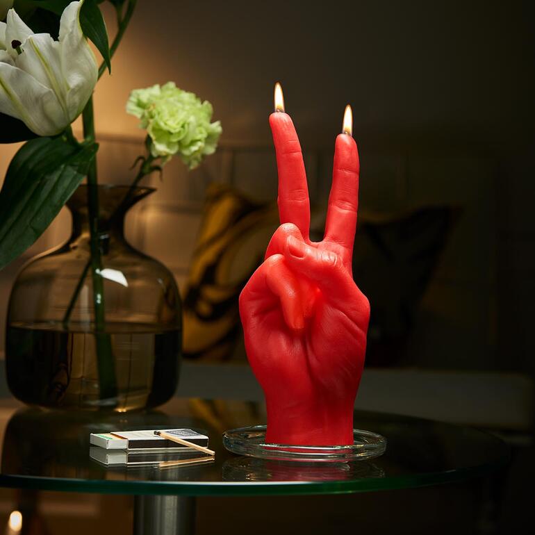 Rote Handgestenkerze in Form eines Friedenszeichens auf einem Tisch.