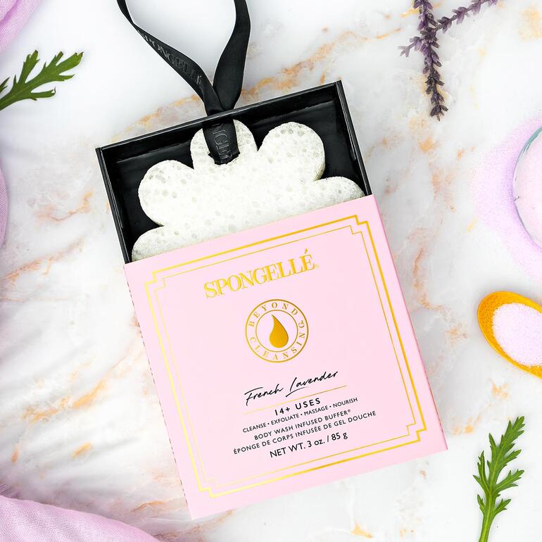 Spongellé Beauty-Schwamm in einer blütenförmigen Verpackung auf einer bunten Dekoration.