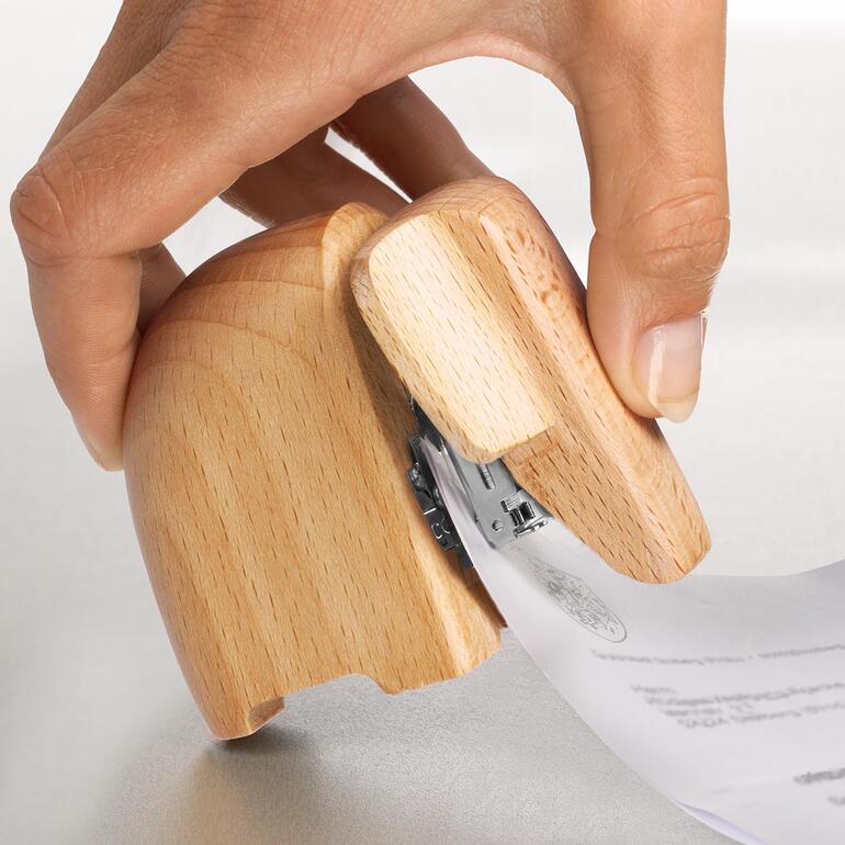 Hand hält Papiere, während sie einen Holz-Elefanten-Heftgerät benutzt.