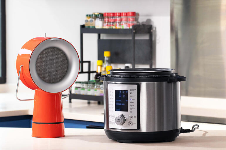 Rote AirHood™ neben einem elektrischen Kochgerät auf einer Arbeitsfläche.