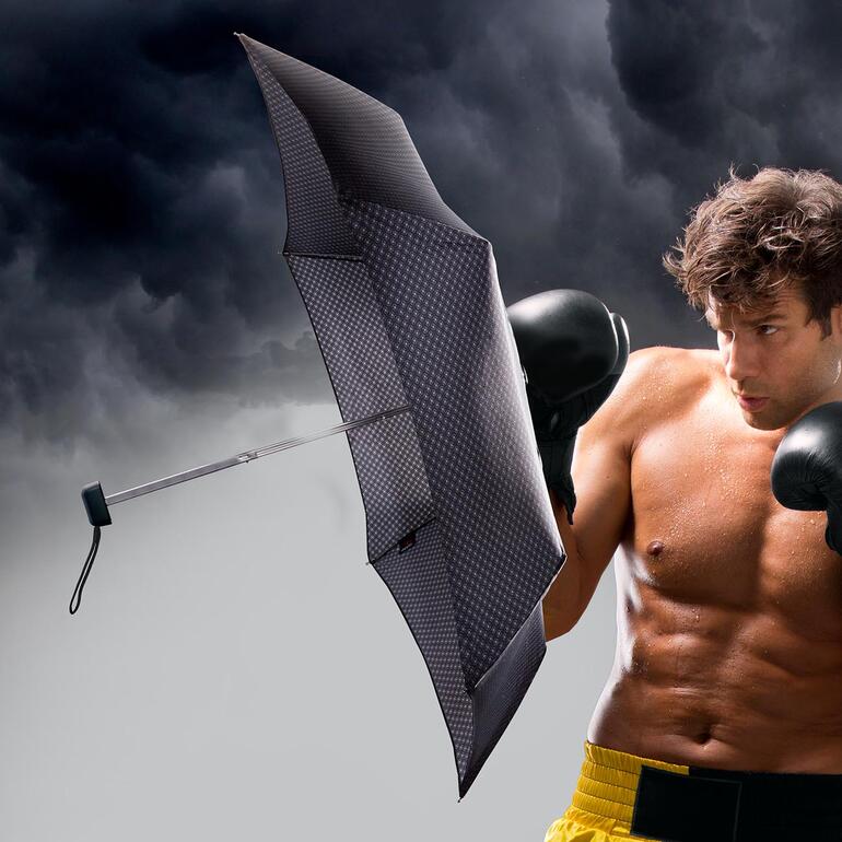 Mann mit Carbonstahl-Taschenschirm in einer stürmischen Umgebung.