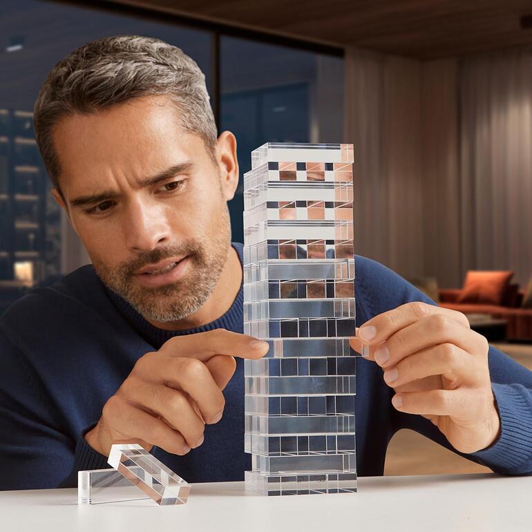 Mann spielt Geschicklichkeitsspiel „Tower“ aus transparenten Blöcken.