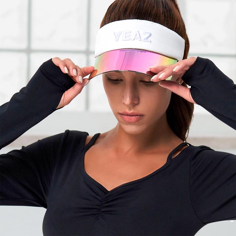 Frau mit Sonnen-Visor hebt sie leicht an, trägt ein schwarzes Oberteil.